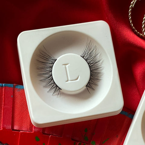 Lithe Lashes Mini Lashes lash style named M2 - Mini Winged, a product image of the lashes in their biodegradable stowing tray, laying overtop red floral silk fabric.