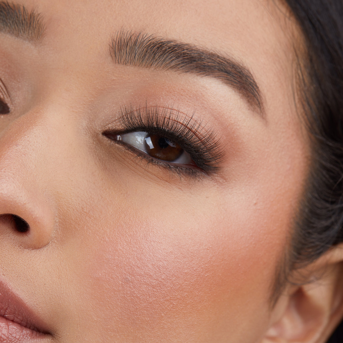Lithe Lashes Core Collection lash style named 04 Long and Graceful, an image of a model’s face wearing lithe lashes on both eyes, with full makeup, looking from a left side profile, semi zoomed in, displaying the elegance of the lashes on her eyes.